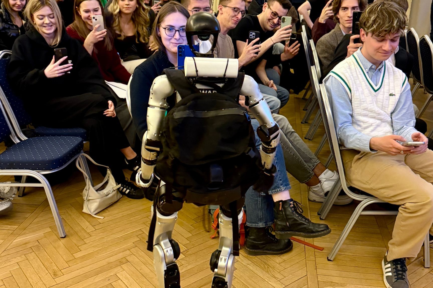 Ben, humanoider Roboter, zwischen Gästen in einem Saal.